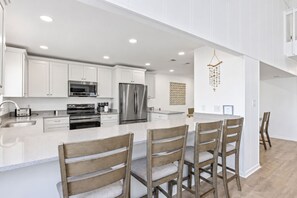 A modern kitchen with white cabinetry, stainless steel appliances, and a central island with bar stools. - The Wave | Entire 10BR Duplex | 2 Private Pools | Steps to Beach (Grayton Beach)