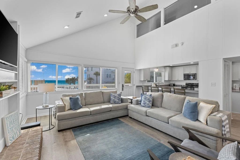 A spacious living area with a large sectional sofa, a ceiling fan, and a view of the ocean through large windows.