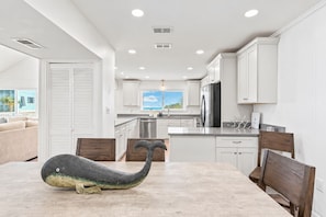 A modern kitchen with white cabinetry, stainless steel appliances, and a dining area with a table and chairs. - The Wave | Entire 10BR Duplex | 2 Private Pools | Steps to Beach (Grayton Beach)