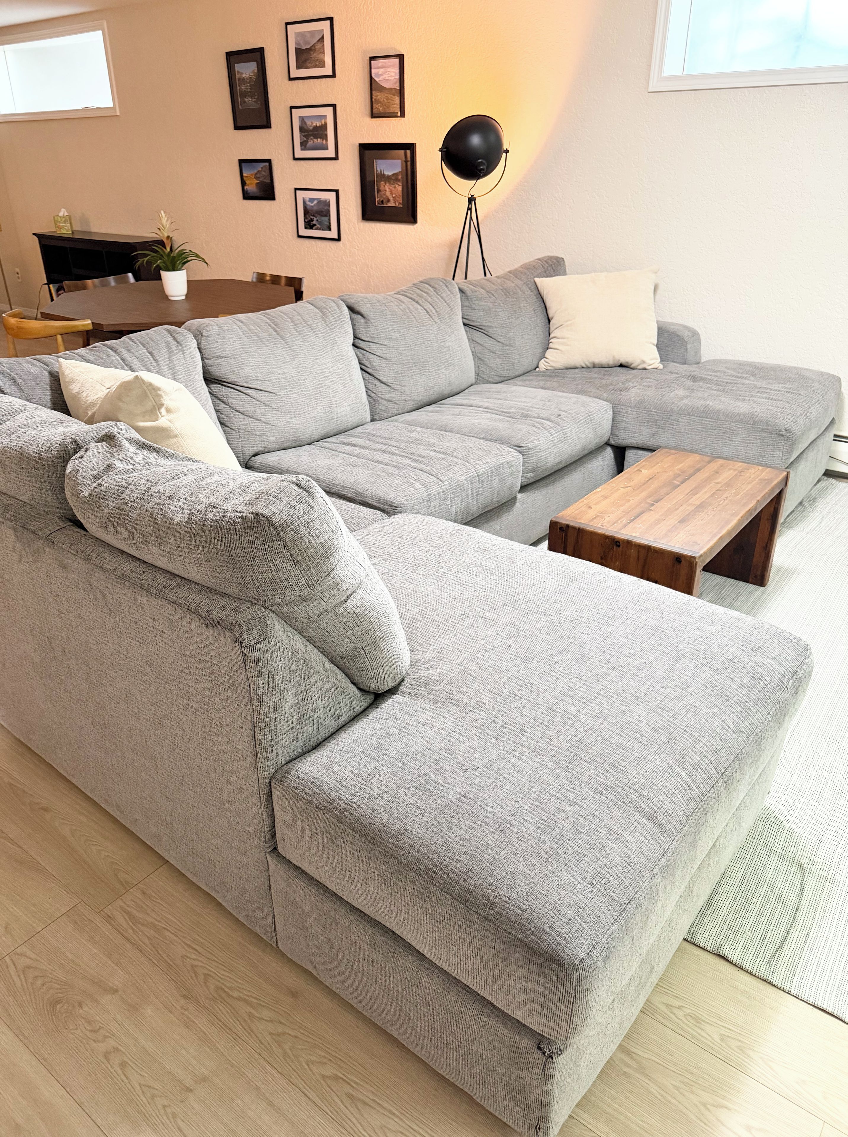 Ein graues Ecksofa mit einem Couchtisch aus Holz und einer Stehlampe in einem Wohnzimmer.