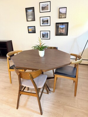 A round wooden dining table with four chairs, a potted plant, and framed pictures on the wall. - Red Rock Ridge- 2 Bedroom Suite (Wheat Ridge)