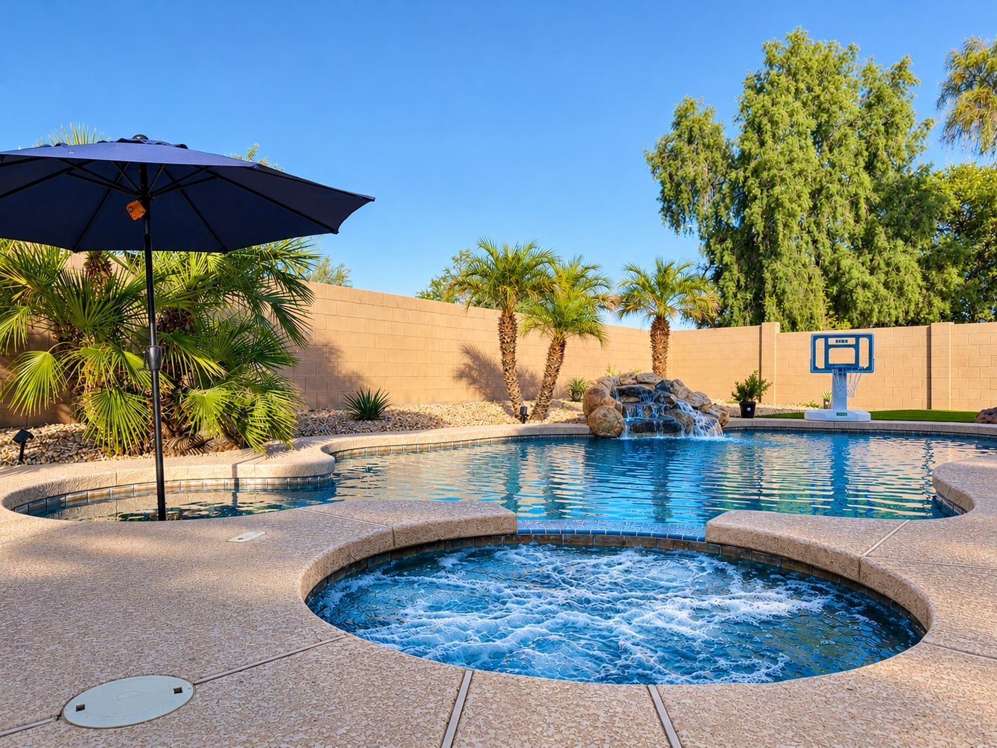 A swimming pool with a hot tub, palm trees, and a basketball hoop.