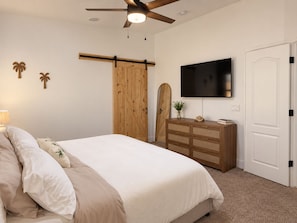 A bedroom with a bed, a dresser, a television, and a ceiling fan.