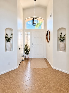 A hallway with a white door, a large window with a view of the sky, and two potted plants on either side. - 1 mile to Spring Training - Backyard Oasis - Pool Hot Tub -4BR Single Level Home (Goodyear)