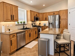 A modern kitchen with wooden cabinets, stainless steel appliances, and a granite countertop. - 1 mile to Spring Training - Backyard Oasis - Pool Hot Tub -4BR Single Level Home (Goodyear)