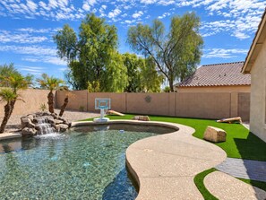A swimming pool with a waterfall feature, surrounded by a brick wall and green artificial turf.