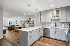 A modern kitchen with grey cabinets, a white countertop, and a dining area with a wooden table and chairs. - Spacious Prospector 3BR | Sleeps 8 | Pool & Hot Tub (Park City)