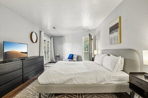 A modern hotel room with a large bed, a flat-screen TV, a dresser, and a view of the outdoors. - Spacious Prospector 3BR | Sleeps 8 | Pool & Hot Tub (Park City)