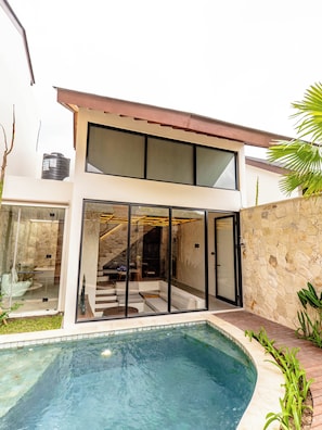 Una casa moderna de dos pisos con piscina, puertas de vidrio amplias y un muro de piedra.