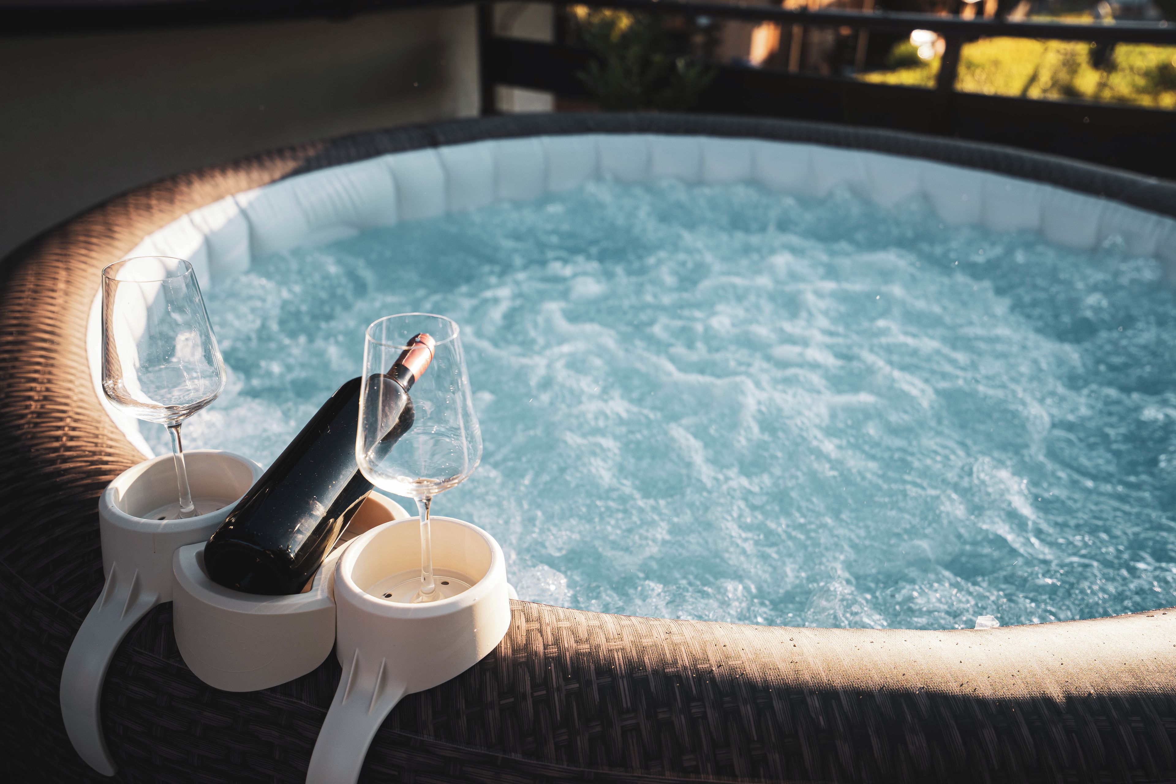 A hot tub with two glasses and a bottle, surrounded by wicker furniture.