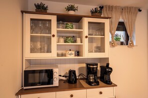 Eine Küche mit Mikrowelle, Kaffeemaschine und Schränken voller Gläser und Küchenutensilien.