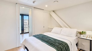 Ein modernes Schlafzimmer mit einem Bett, einem Nachttisch mit Lampe und Blick ins Freie durch eine Schiebetür.