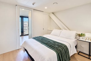 A modern bedroom with a bed, a bedside table with a lamp, and a view of the outside through a sliding door. - Te Aro City Apartment - 1BR with Pool & Gym (Wellington)