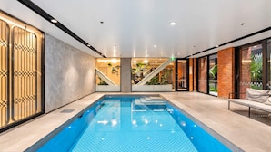 Ein moderner, überdachter Schwimmbereich mit klarem Wasser, umgeben von einem minimalistischen Design mit Treppe und Sitzgelegenheit.