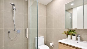 Ein modernes Badezimmer mit einer Duschkabine, einer weißen Toilette und einem hölzernen Waschtisch mit Waschbecken und Spiegel.