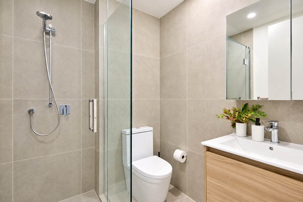 Modern bathroom with a glass-enclosed walk-in shower, adjustable handheld showerhead, toilet, vanity sink, storage cabinet and large mirror at Alpha Street 808.