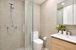 A modern bathroom with a glass-enclosed shower, a white toilet, and a wooden vanity with a sink and mirror. - Te Aro City Apartment - 1BR with Pool & Gym (Wellington)
