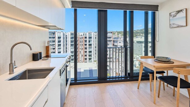 Eine moderne Küche mit großem Fenster, einem Essbereich mit Tisch und Stühlen sowie Blick auf hohe Gebäude.