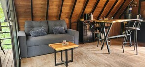 A cozy loft with a sofa, a small table, a kitchen area with a bar, and a wooden ceiling. - Bird House Ecolodge (Barbosa)
