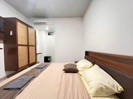Quarto de hotel com cama, almofadas, cabeceira de madeira, guarda-roupa e ar condicionado.