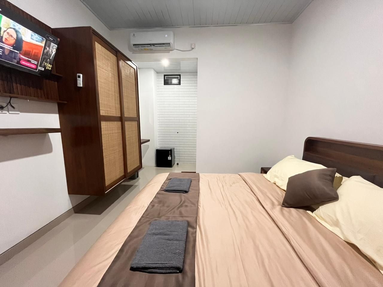 Habitación de hotel con cama, almohadas, televisor, armario y aire acondicionado.