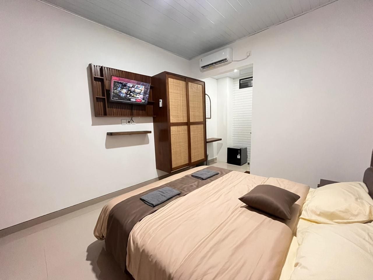 A hotel room with a bed, a television mounted on the wall, and a wardrobe.