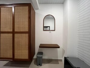 A room with a wooden wardrobe, a small mirror, a wooden shelf, and a trash bin. - You & Me Guesthouse By GUMA (Denpasar)