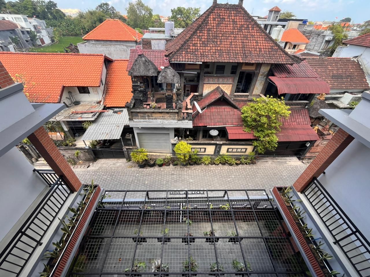 Un patio con una estructura de techo de paja, un edificio de tejas rojas y un área vallada con plantas.
