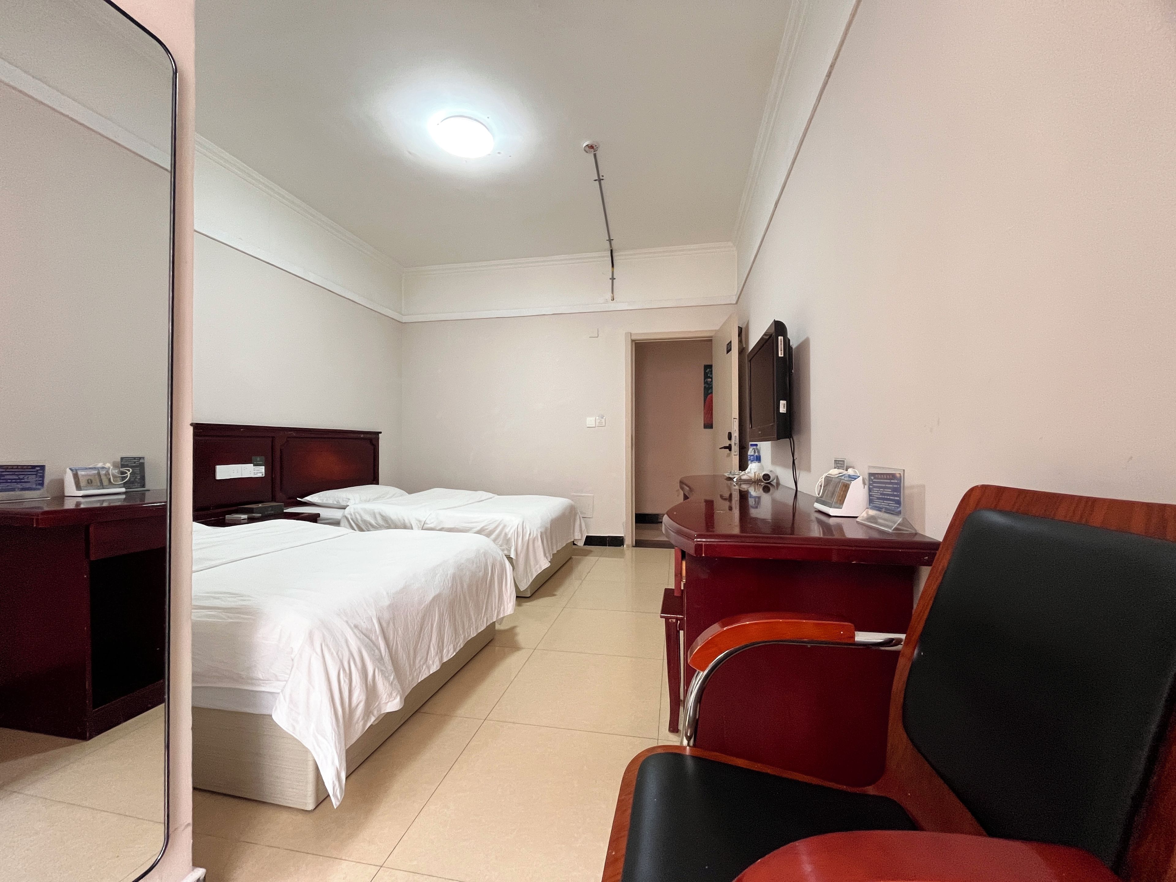 Quarto de hotel com duas camas, uma mesa, uma cadeira e uma televisão.