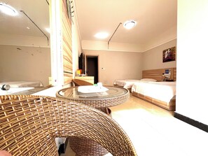 Une chambre d’hôtel avec un canapé rond en osier, un lit avec une tête de lit en bois et une petite table ronde.
