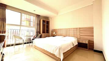 Habitación de hotel con una cama grande, un armario de madera, una zona de estar con sillas y una ventana con cortinas.