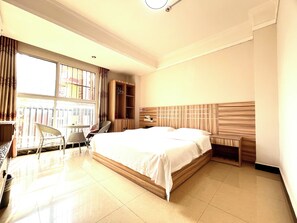 A hotel room with a large bed, a wooden wardrobe, a seating area with chairs, and a window with curtains. - MAXHILL INN (Splashing Square) (Xishuangbanna Dai)