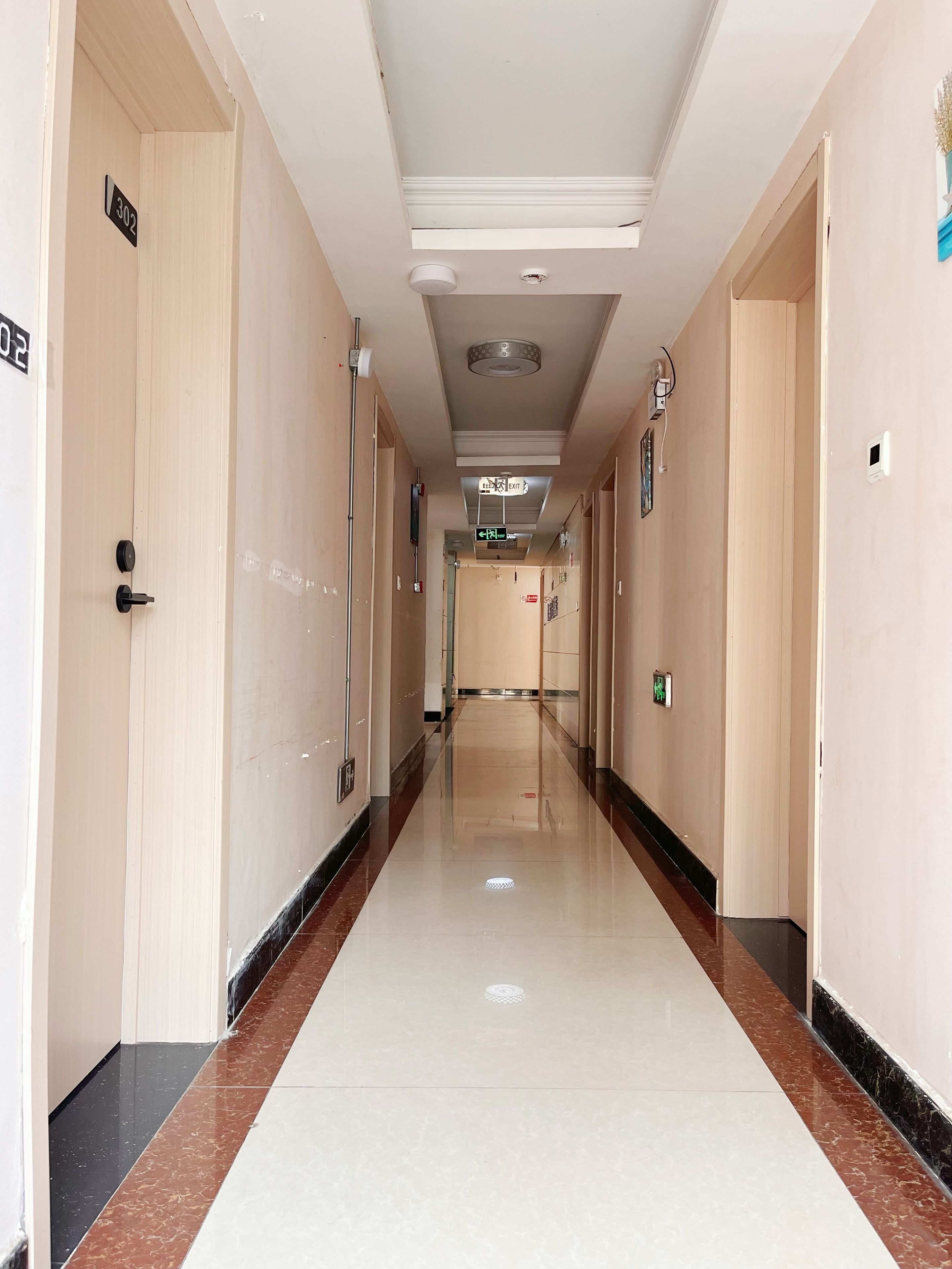 A hotel corridor with a polished floor, doors on both sides, and an exit sign overhead.