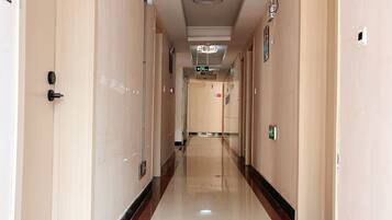 A hotel corridor with a polished floor, doors on both sides, and an exit sign overhead.
