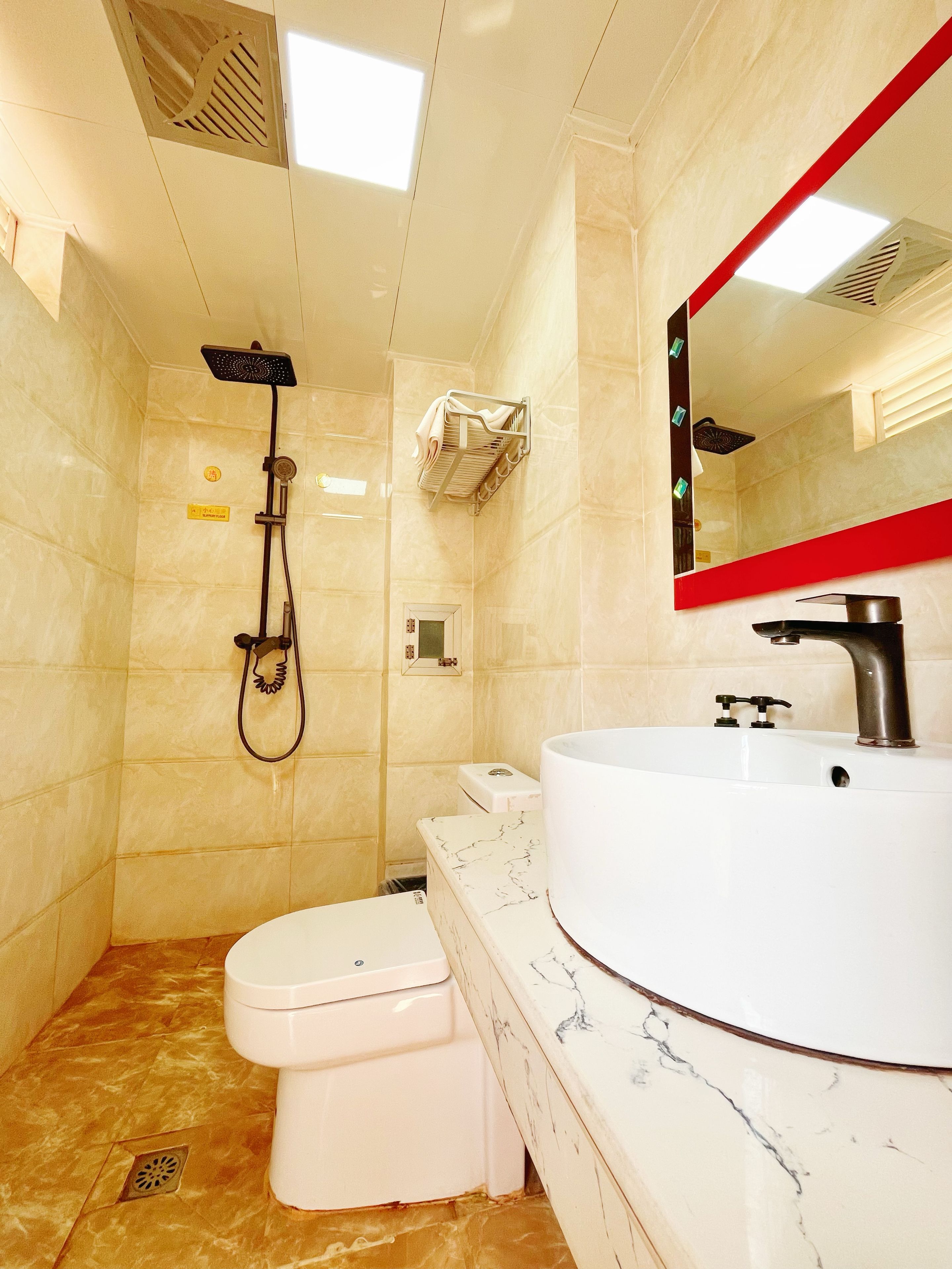 A bathroom with a white sink, a toilet, a showerhead, and a mirror with a red frame.