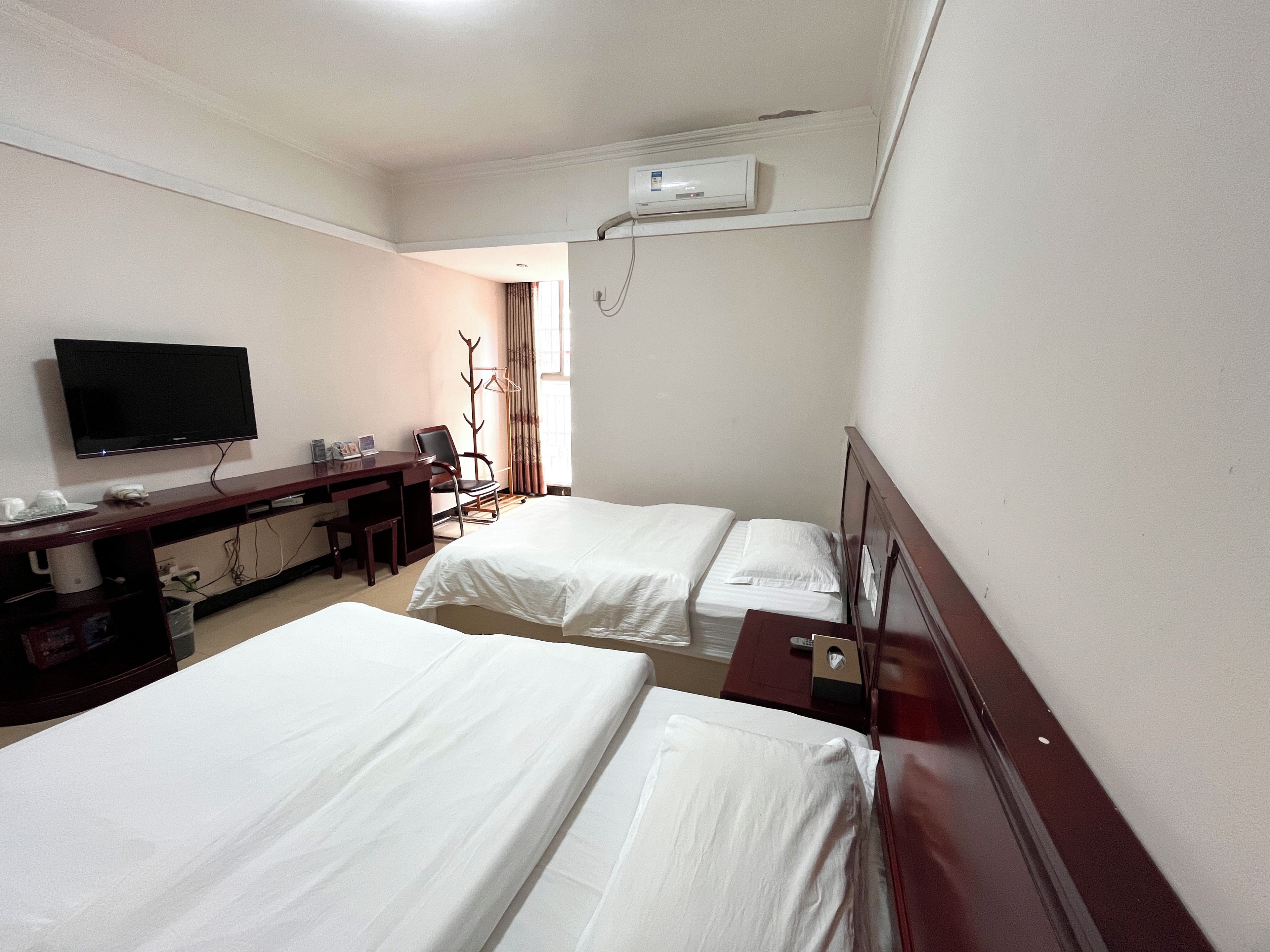 A hotel room with two beds, a desk with a flat-screen TV, a chair, and a wardrobe.