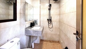 Un baño con lavamanos de mármol, un espejo, ducha con cabezal de ducha manual y un inodoro.
