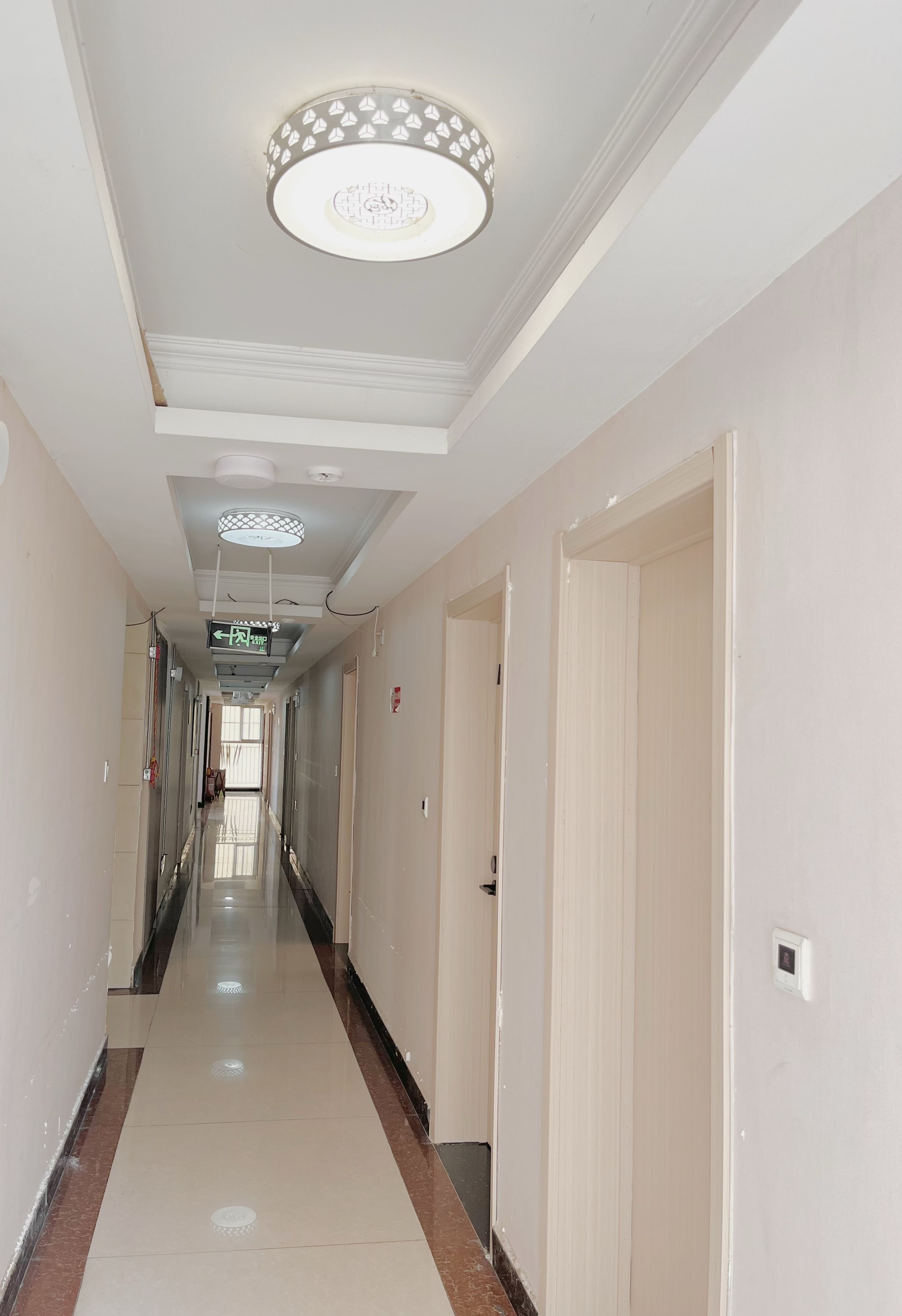 A hotel corridor with doors on both sides, a tiled floor, and a ceiling with decorative light fixtures.