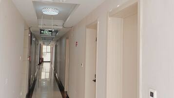 A hotel corridor with doors on both sides, a tiled floor, and a ceiling with decorative light fixtures.
