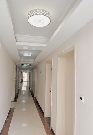 Un pasillo de hotel con puertas a ambos lados, suelo de baldosas y techo con luminarias decorativas.