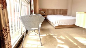 Una habitación de hotel con cama, mesita de noche, una silla y una ventana con cortinas.