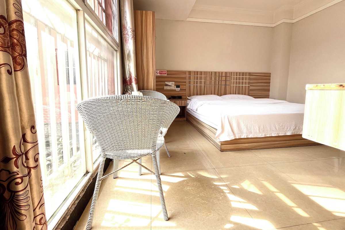 Una habitación de hotel con cama, mesita de noche, una silla y una ventana con cortinas.