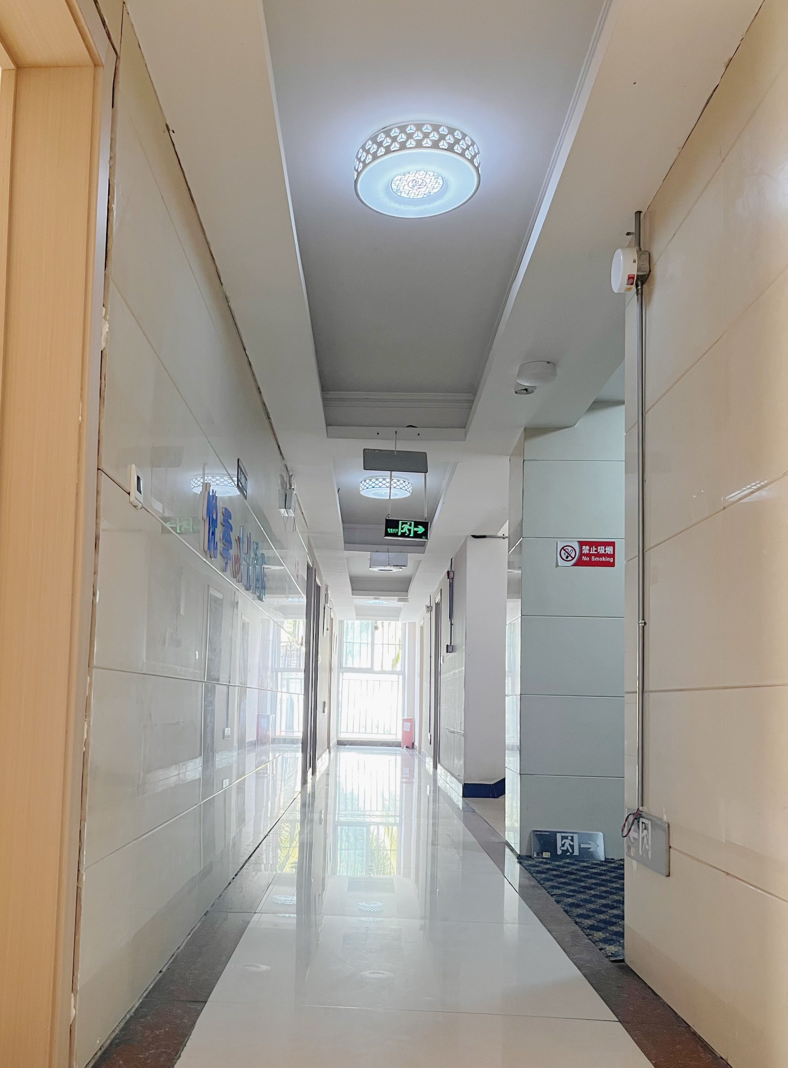 A clean, well-lit hallway with a 'No Smoking' sign, directional signs, and a tiled floor.