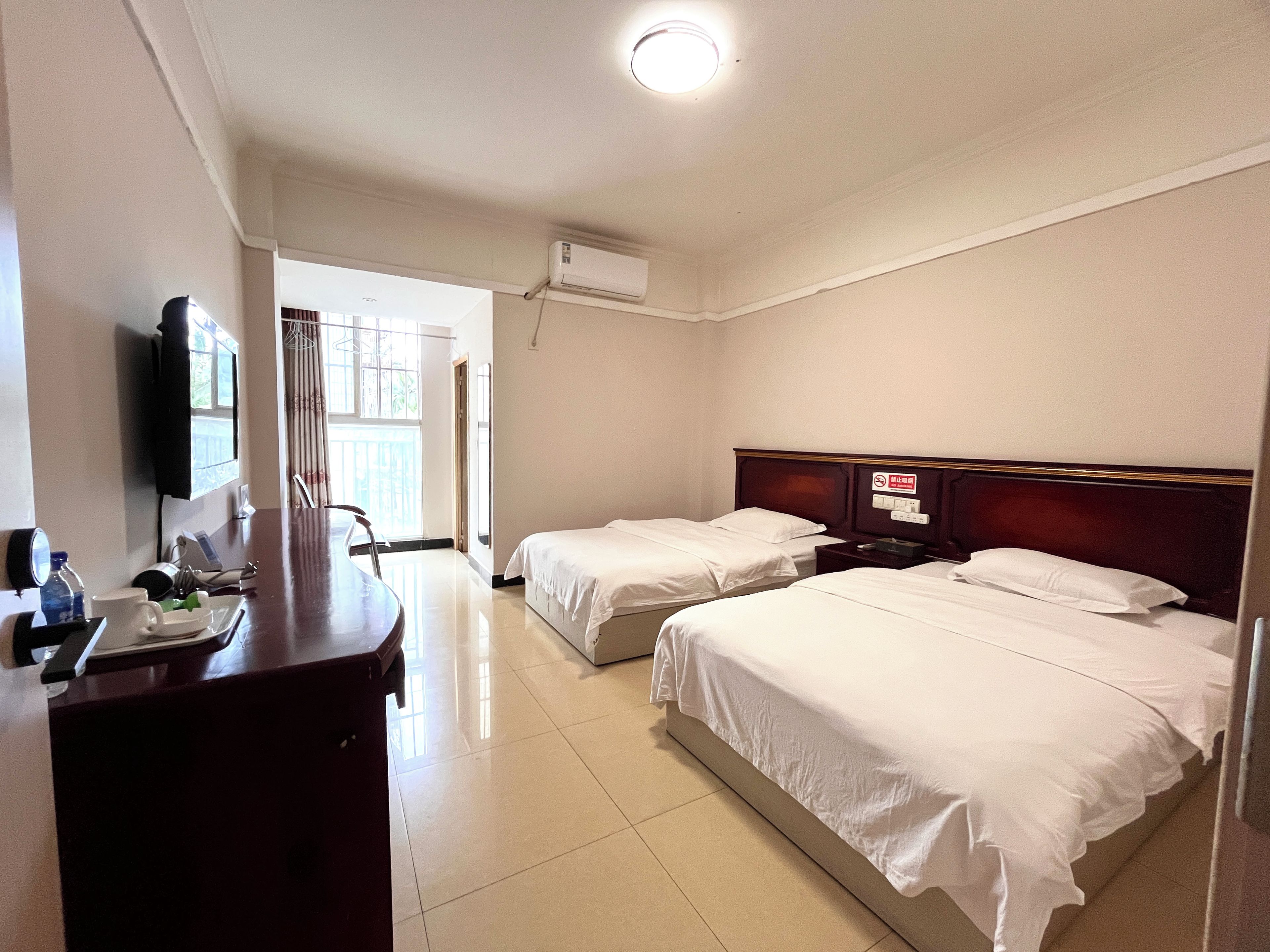 Una habitación de hotel con dos camas, un escritorio con silla, un televisor y una ventana.