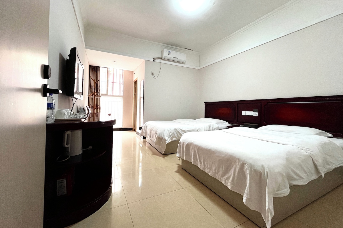 Habitación de hotel con dos camas, un escritorio con silla, un televisor de pantalla plana y un aire acondicionado.