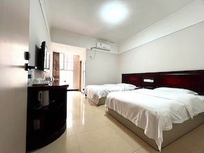 Habitación de hotel con dos camas, un escritorio con silla, un televisor de pantalla plana y un aire acondicionado.