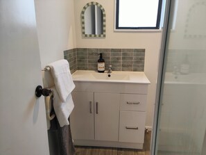 A bathroom with a white sink, a mirror with a green frame, and a towel hanging on a door handle. - Fresh, Cosy & Handy to CBD, Lake, Waikato Hospital, Gym (2) and Dinsdale Shops (Hamilton)