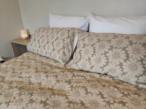 A bed with a floral patterned bedspread, a bedside lamp, and a nightstand with a bottle. - Fresh, Cosy & Handy to CBD, Lake, Waikato Hospital, Gym (2) and Dinsdale Shops (Hamilton)