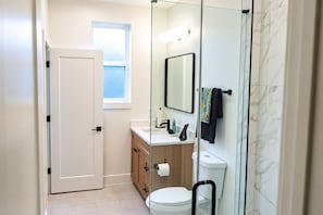 Une salle de bain moderne équipée de toilettes, d’un lavabo et d’une douche à parois de verre.