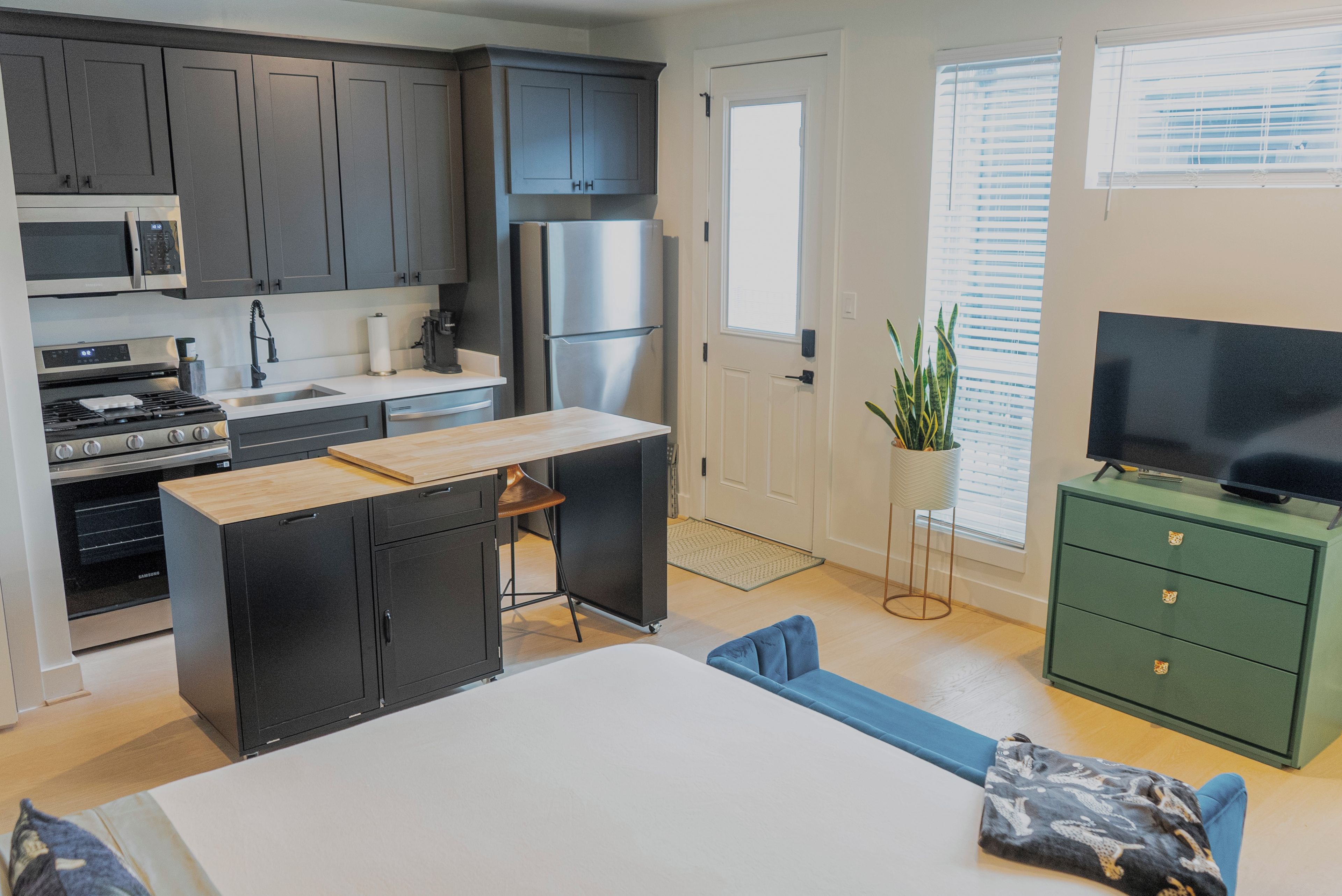 A compact kitchen with modern appliances, a dining area with a table and chairs, and a green cabinet with a television.